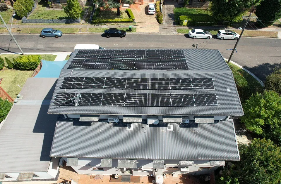 A drone view of a finished rooftop solar array covering most of a suburban house roof, with the street and neighbouring homes below.