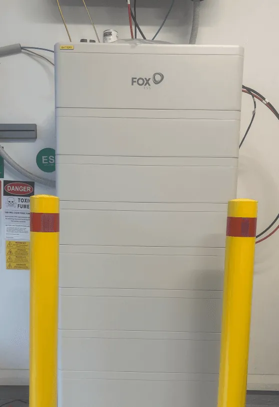 A Fox ESS battery stack against an internal wall, with two yellow impact bollards in front of it and the battery isolator above.