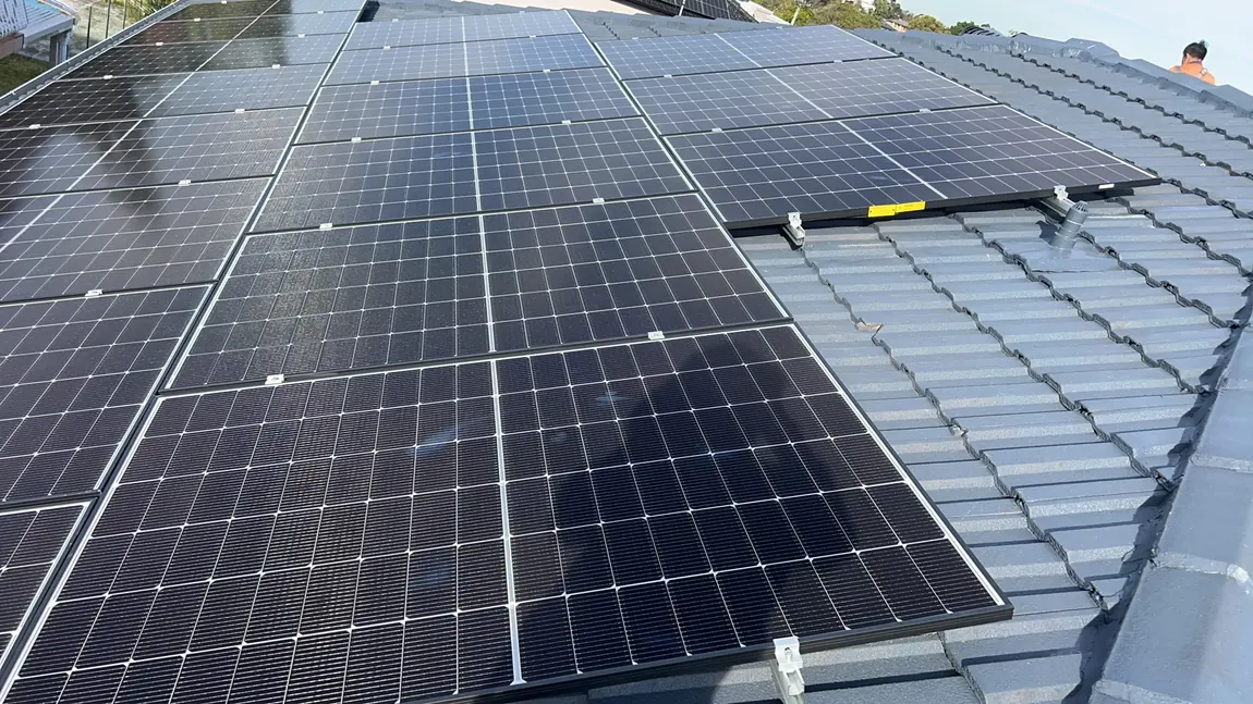 Solar panels landed and clamped to their rails across a tile roof, photographed along the plane of the array.